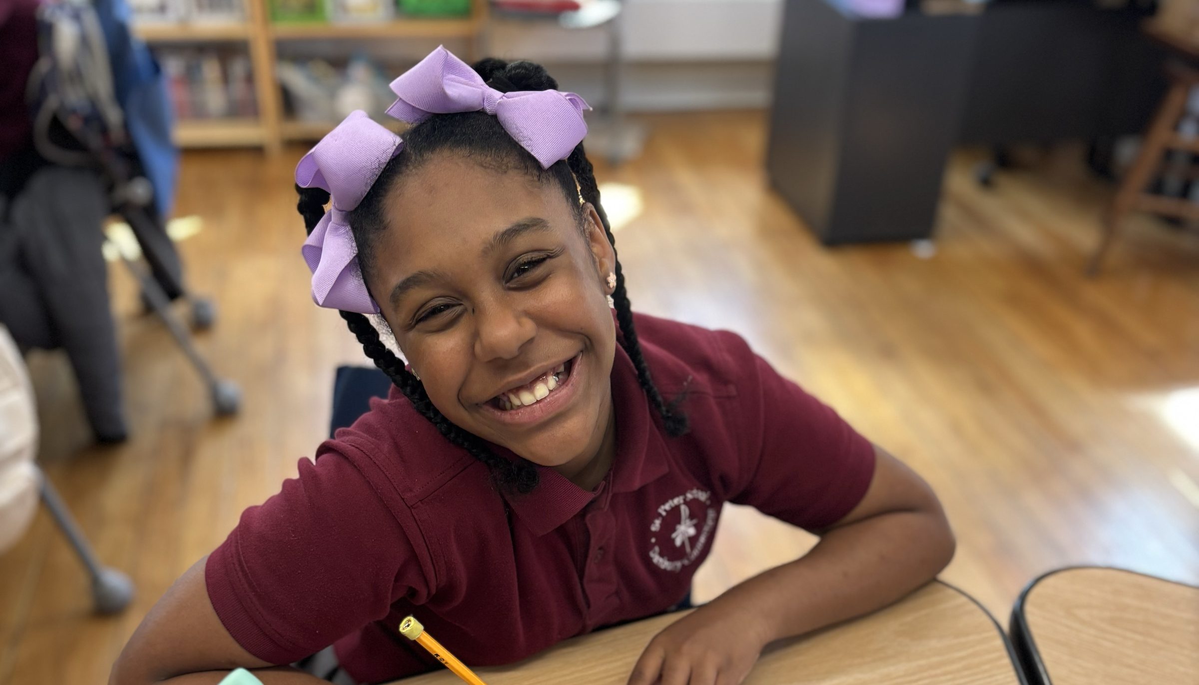 A smiling scholarship student writing at her desk in a Catholic school classroom